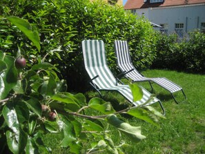 Zwei gestreifte Liegestühle in einem Garten, im Hintergrund ein weißes Gebäude.