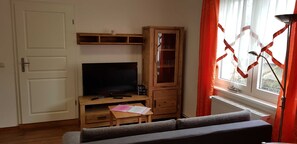 Un salon avec un téléviseur, un meuble en bois et une fenêtre avec des rideaux.
