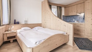 Un dormitorio con cama de madera, mesita de noche y lámpara. Hay una ventana con cortinas y vistas al exterior.