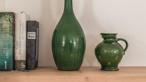 Una estantería de madera con un jarrón verde alto y una jarra pequeña verde con motivos florales, junto a una hilera de libros.