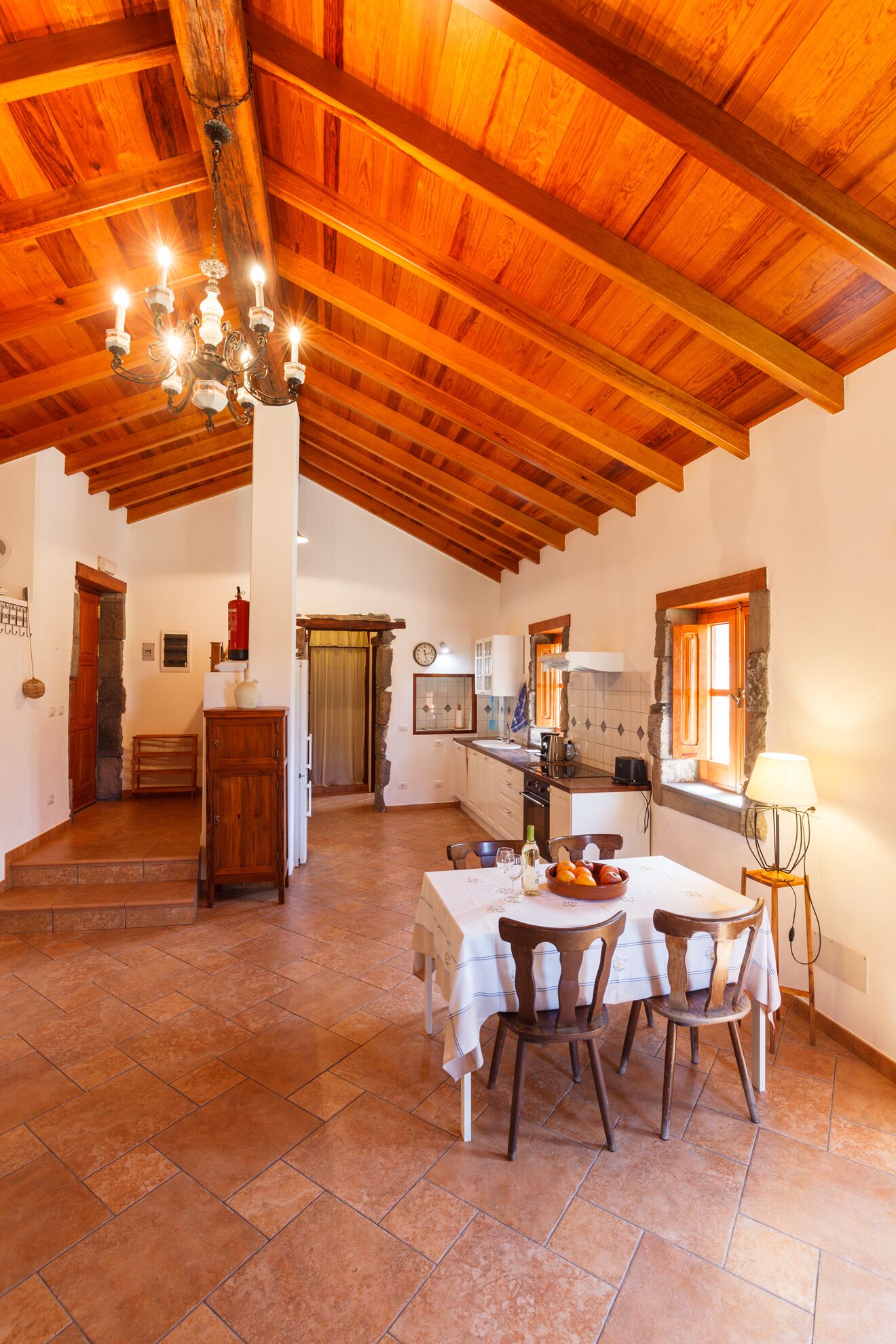 A spacious kitchen with wooden beams, a dining area with a table and chairs, and a stone fireplace.