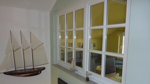 Une pièce dotée d’une grande fenêtre, d’une maquette de voilier fixée au mur et d’un tableau encadré.
