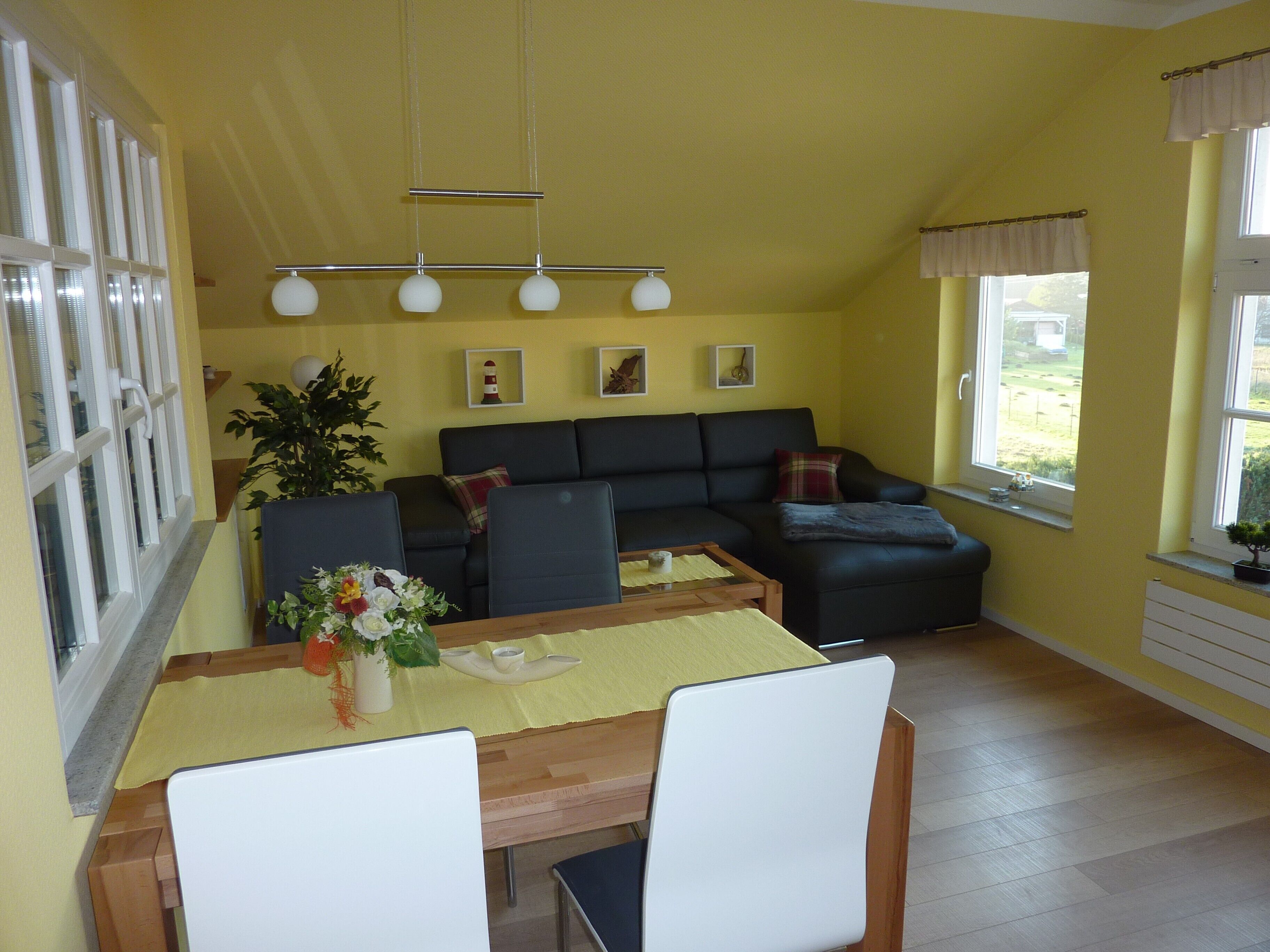 A living room with a sofa, a dining table with chairs, a potted plant, and a window with curtains.