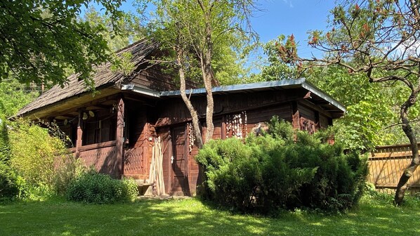 Eine rustikale Holzhütte mit geneigtem Dach, umgeben von üppigem Grün und Bäumen.