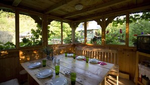 Un comedor de madera con una mesa dispuesta para cuatro, rodeado de ventanas amplias que dan a un jardín y una casa.