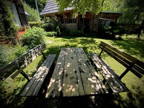 Ein Holztisch mit Bänken in einem Garten, im Hintergrund ein Haus.