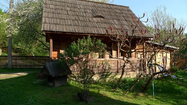 A wooden cabin with a sloped roof, surrounded by lush greenery and a small garden area.