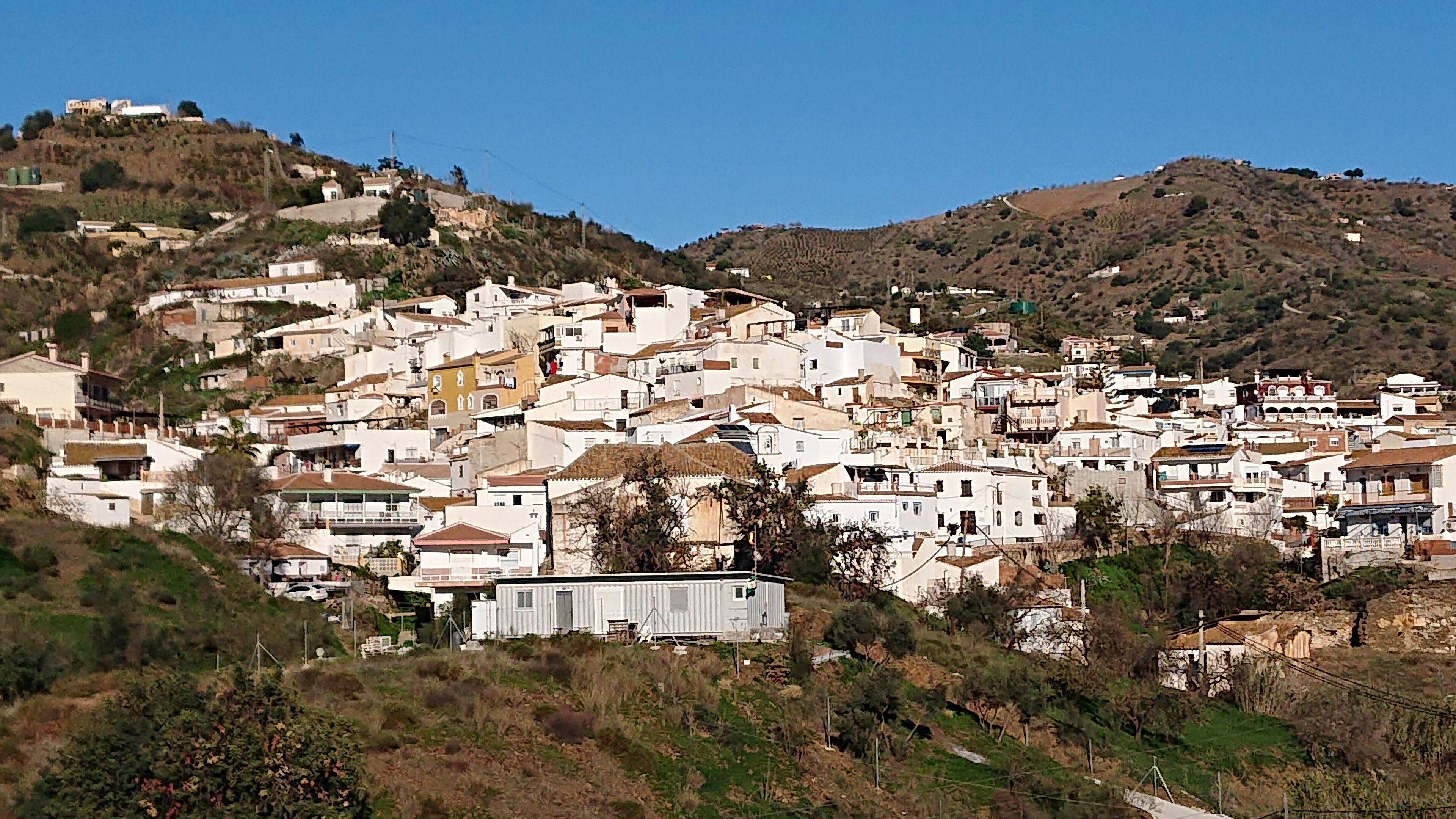 A densely packed hillside town with white buildings, some with balconies, and a few structures on the hilltops.