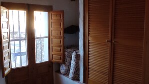 A room with a bed, a window with open shutters, a wooden wardrobe, and a bench with cushions. - Rustic apartment in the Andalusian village of Cajiz (Cajiz)