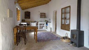 A rustic interior with a wooden dining table, chairs, a kitchen area, and a wood-burning stove. - Rustic apartment in the Andalusian village of Cajiz (Cajiz)