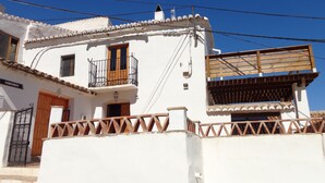 A white building with a balcony, a wooden door, and a metal gate. - Rustic apartment in the Andalusian village of Cajiz (Cajiz)