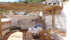 A covered patio with a table and chairs, a pergola, and a view of buildings in the background. - Rustic apartment in the Andalusian village of Cajiz (Cajiz)