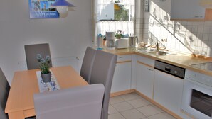 Eine moderne Küche mit einem Holztisch, grauen Stühlen, einer Kaffeemaschine und einem Geschirrspüler.