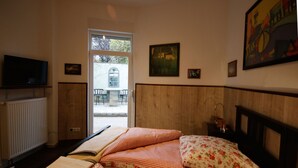 Une chambre d’hôtel avec un lit, un téléviseur posé sur une étagère, une fenêtre et une porte donnant sur un espace extérieur.