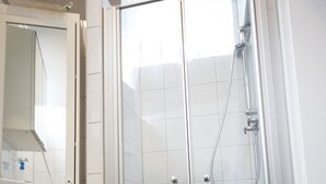 Une salle de bain dotée d’une douche à parois de verre, de carreaux blancs et d’un espace lavabo bien visible.