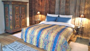 Camera da letto con testiera in legno, copriletto floreale, due lampade ai comodini e un mobile decorativo.