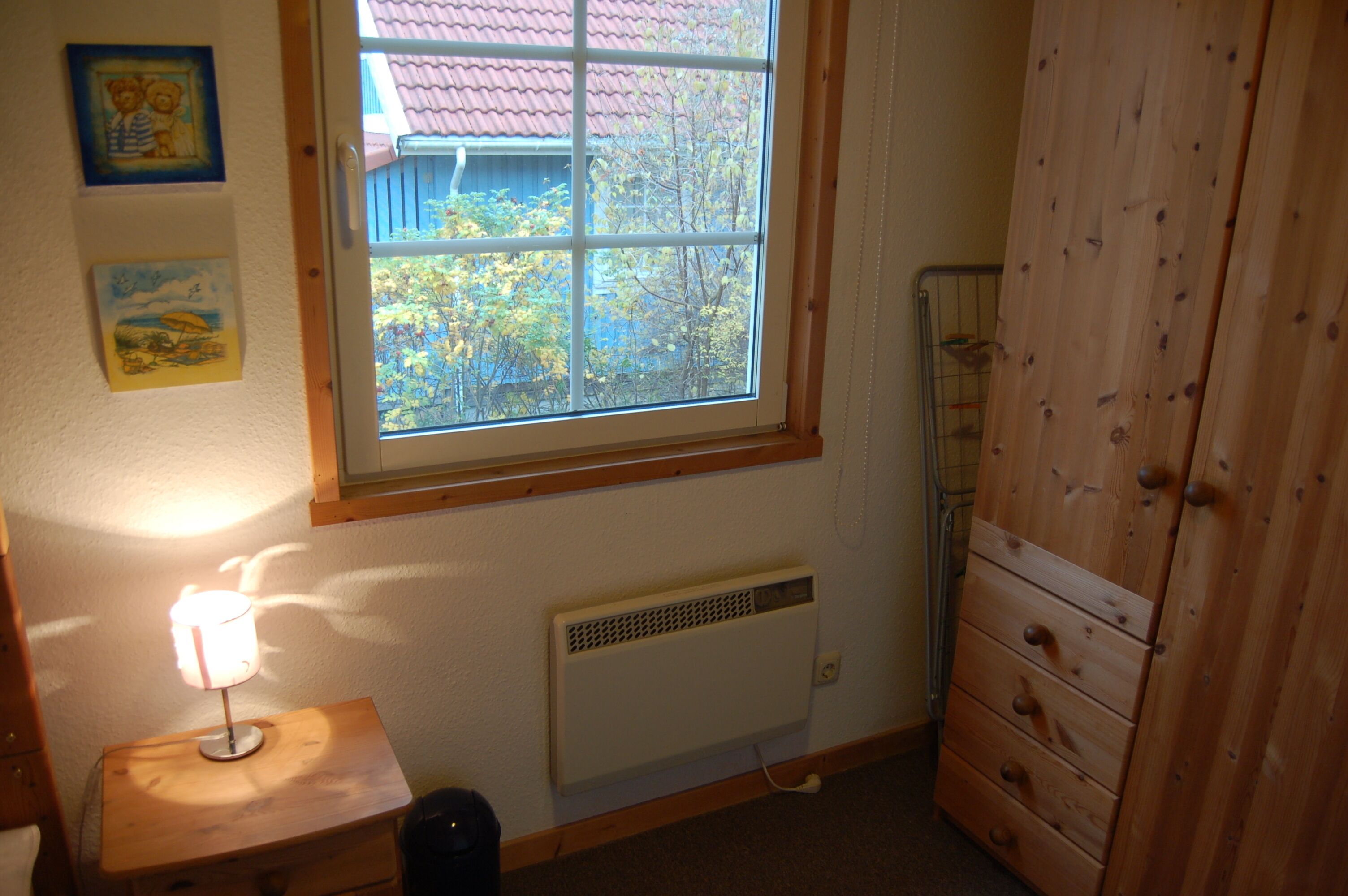 A room with a window, a radiator, a wooden cabinet, and a lamp on a small table.