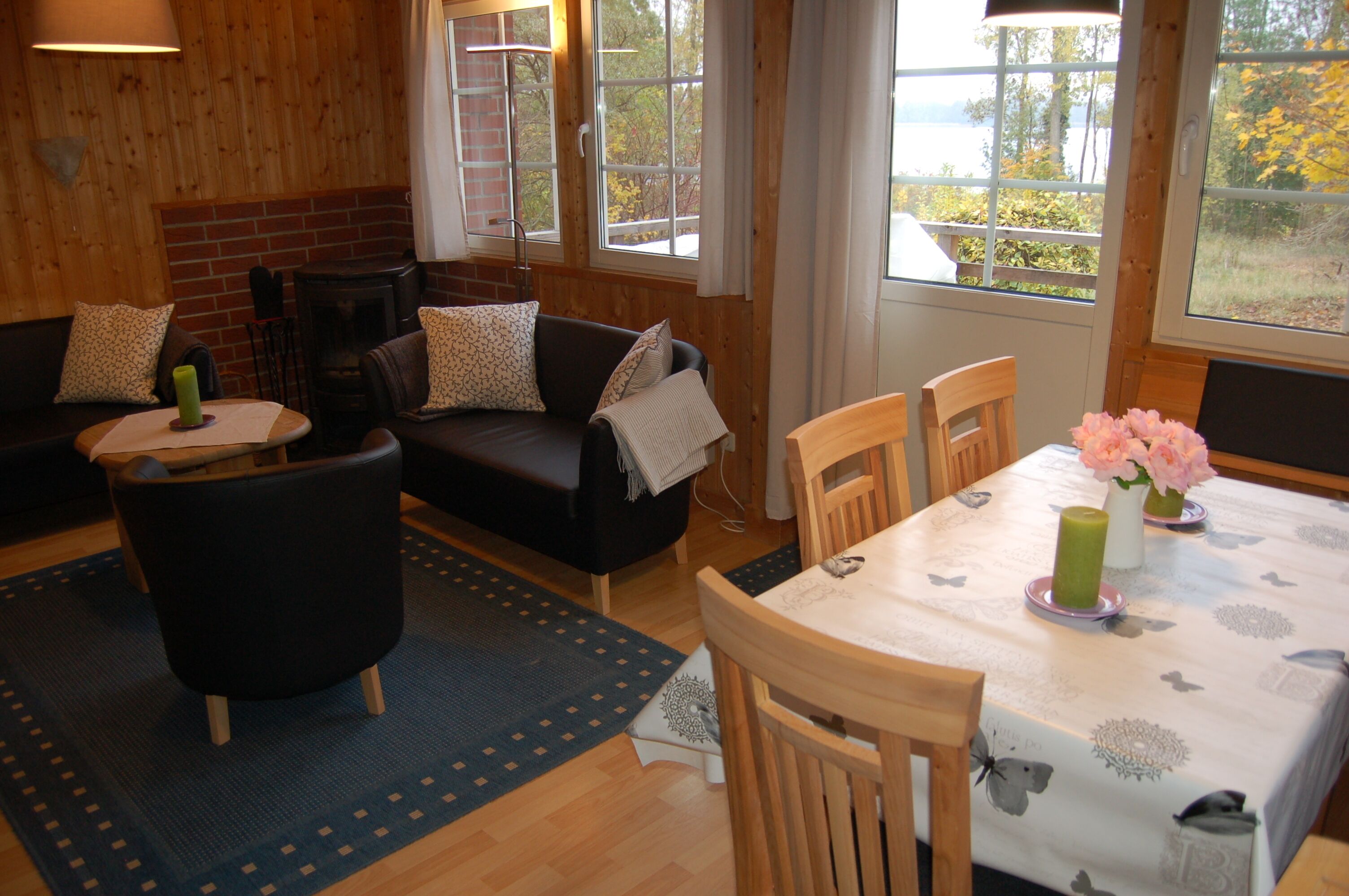 Une pièce chaleureuse avec une cheminée, un canapé, une table à manger avec des chaises et de grandes fenêtres donnant sur l’extérieur.