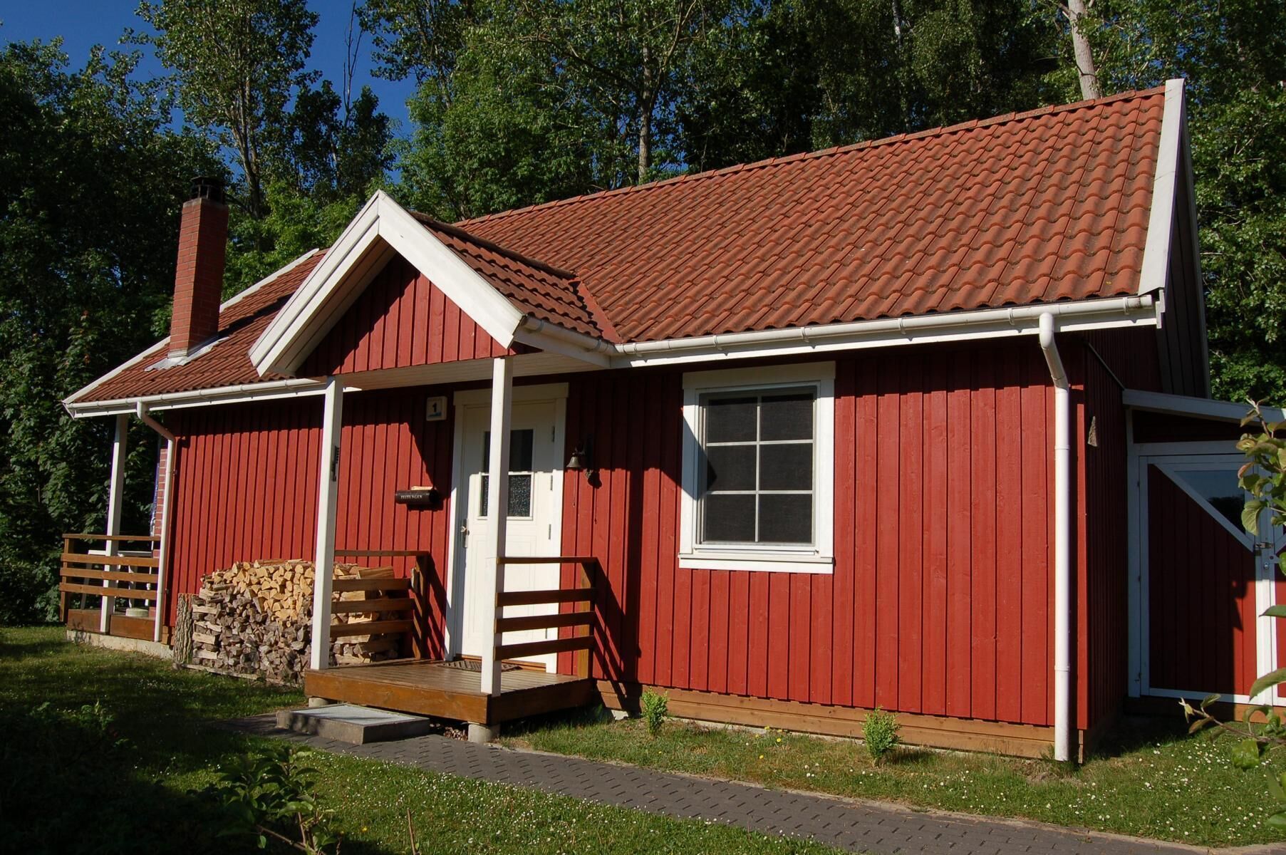 Une maison en bois rouge avec une porte blanche, un petit porche et une cheminée.