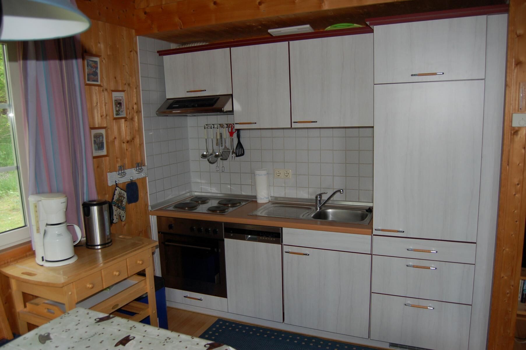 Una cocina compacta con armarios blancos, un lavamanos de acero inoxidable y lavavajillas.