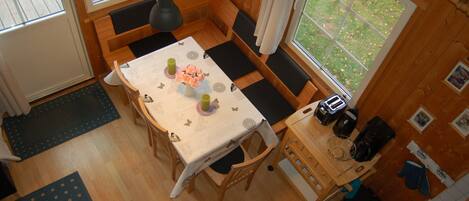 A cozy wooden cabin with a dining table set for four, a bench seating area, and a kitchen counter with appliances.