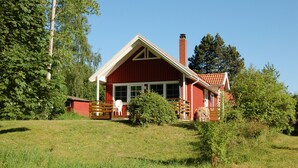 Una casa di legno rossa con un camino, circondata da vegetazione e alberi.