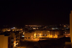 A nighttime view of a cityscape with illuminated buildings and a well-lit parking area.