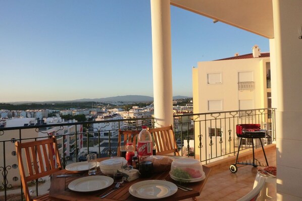 A balcony with a table set for dining, a bottle of Coca-Cola, and a grill.