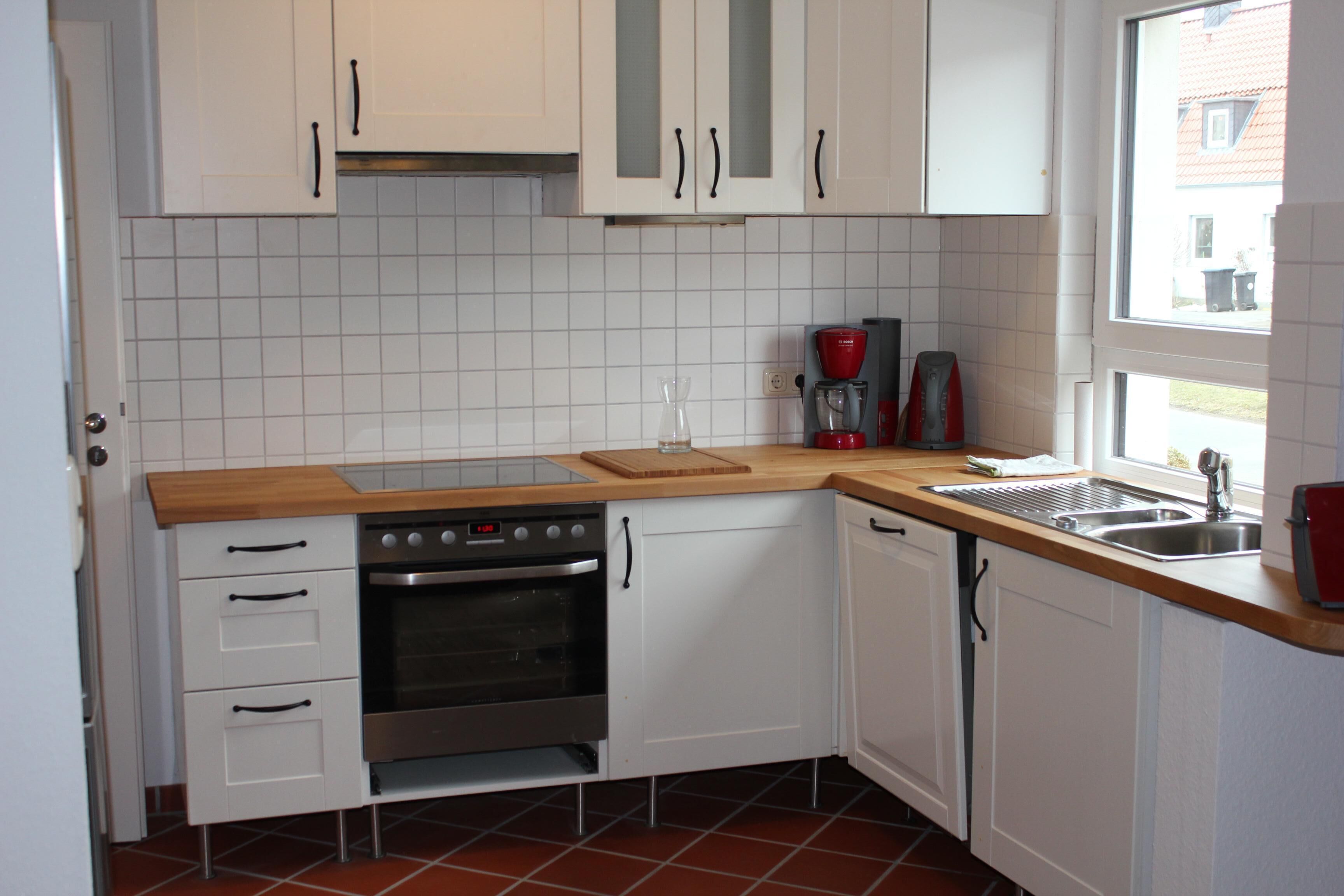 A kitchen with white cabinets, a stainless steel oven, a coffee maker, and a window.