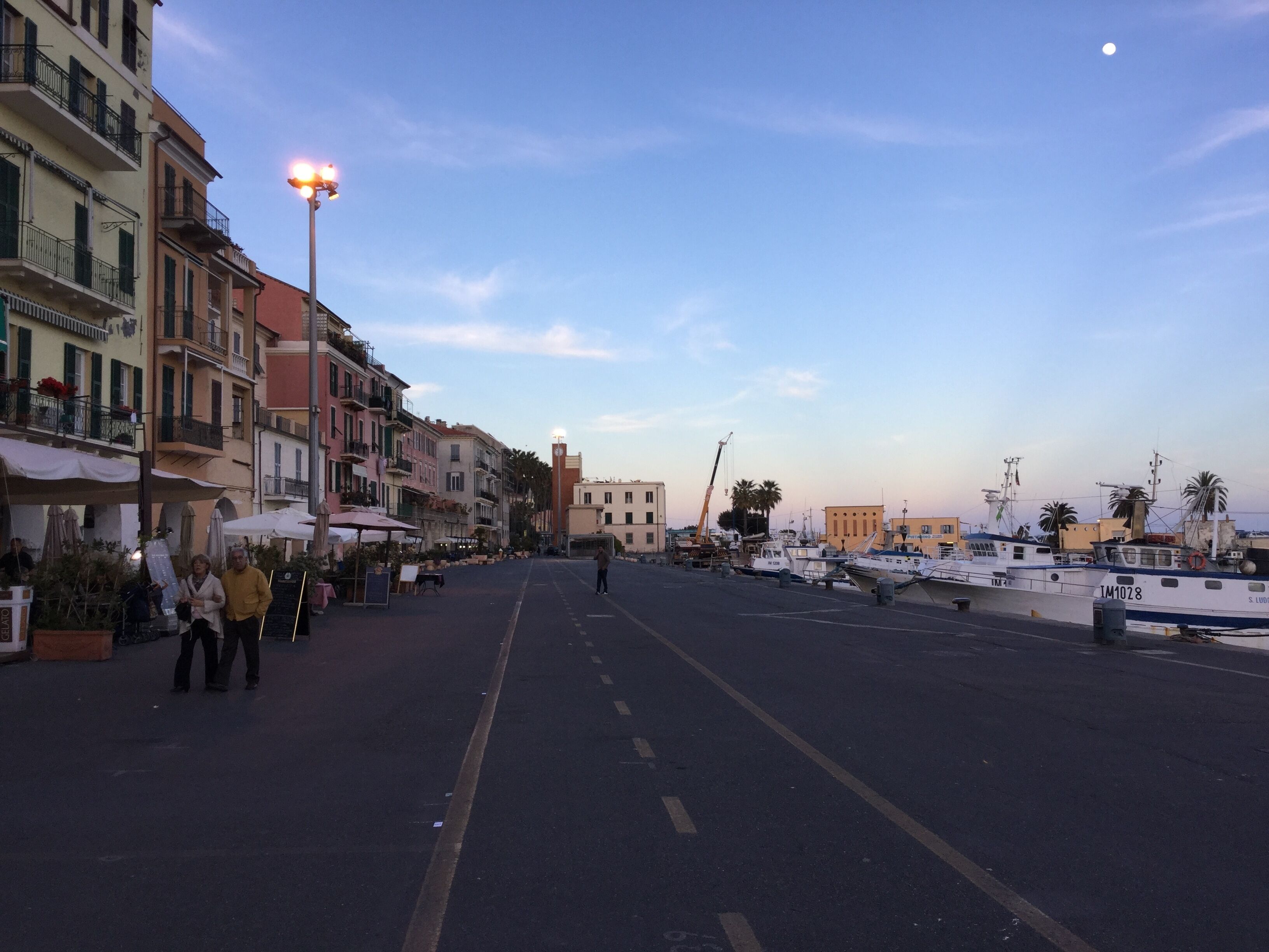Une rue bordée de bâtiments, donnant sur le port, avec un ciel dégagé et des bateaux amarrés.