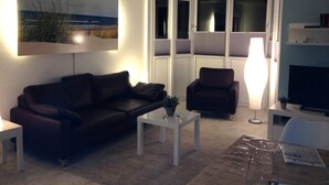 A living room with a dark brown sofa, a white coffee table, a floor lamp, and a television on a stand. - TOP HOLIDAY APARTMENT 65 SQM WITH 2 BEDROOMS, WLAN, balcony (Grömitz)