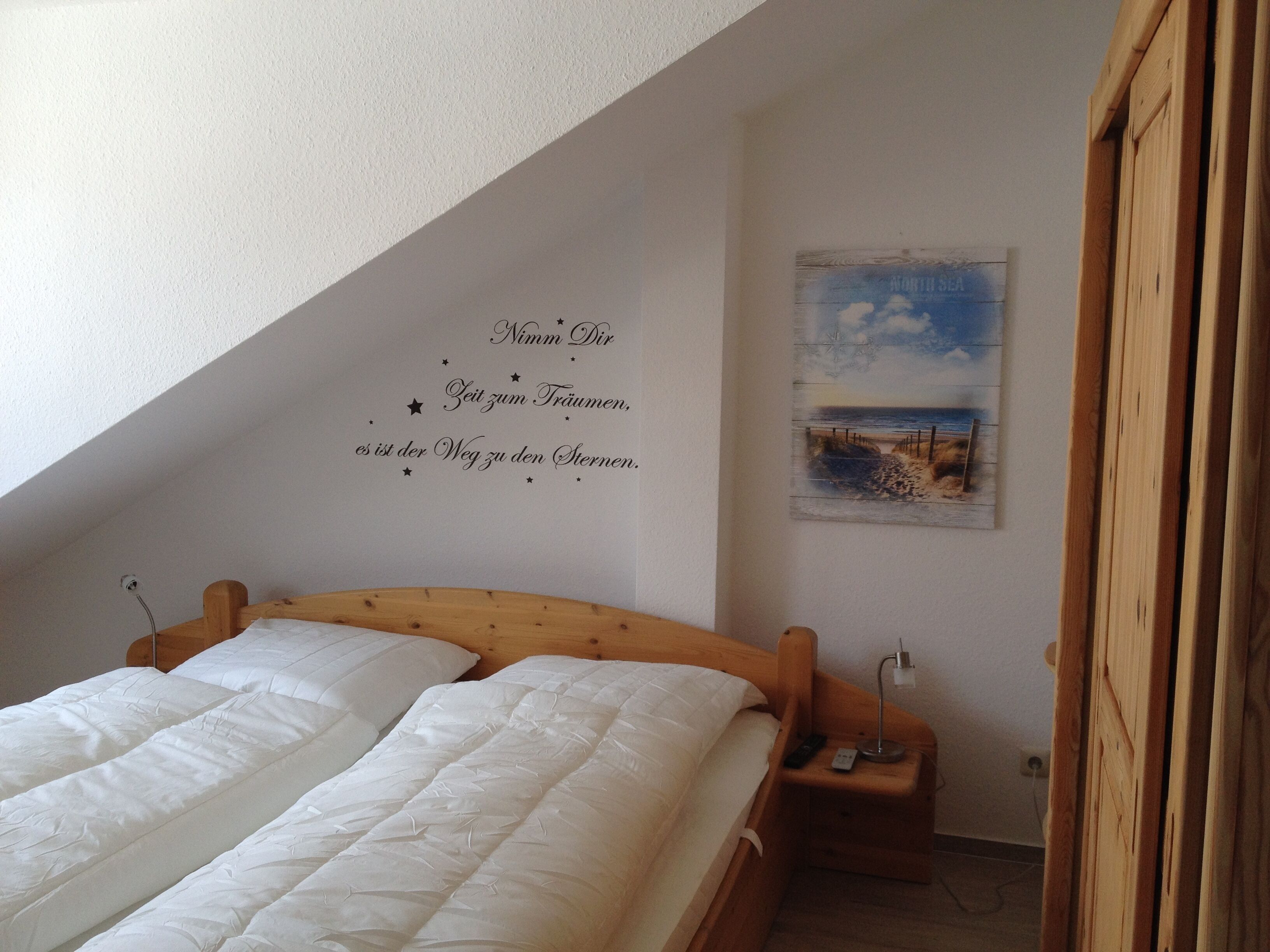 Ein Schlafzimmer mit einem hölzernen Bett, einem Nachttisch, einer Wanddekoration mit Text und einem Gemälde einer Strandansicht.