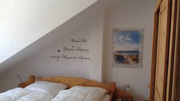Ein Schlafzimmer mit einem hölzernen Bett, einem Nachttisch, einer Wanddekoration mit Text und einem Gemälde einer Strandansicht.