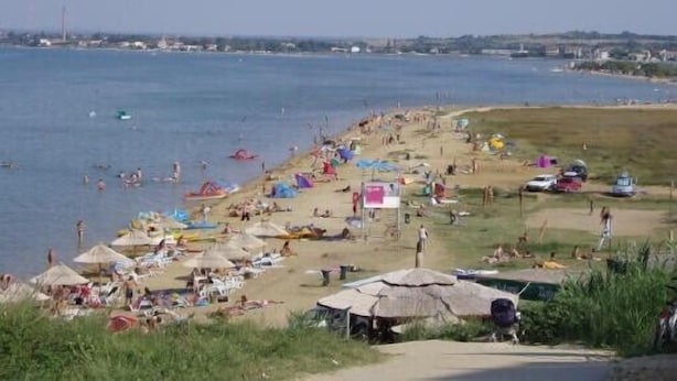 A beach with people sunbathing and swimming, tents, and a few vehicles.