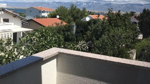A balcony with a view of a residential area, including houses with satellite dishes, trees, and distant mountains.
