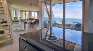 Cozinha moderna com uma ilha grande, área de jantar com mesa e cadeiras, e vista para o oceano através de janelas amplas.