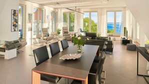 Un vaste espace de vie comprenant une grande table à manger, des sièges confortables et une vue sur la mer.
