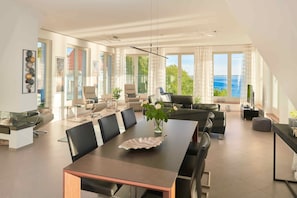 Uma sala de estar ampla com uma grande mesa de jantar, assentos confortáveis e vista para o mar.