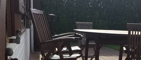 An outdoor patio area with a wooden table and chairs, a potted plant, and a metal bench.