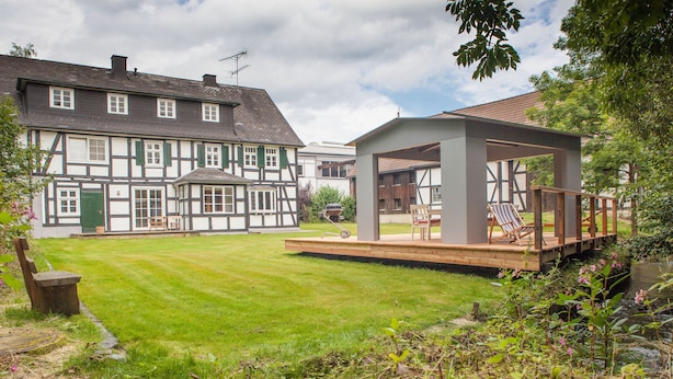 A traditional half-timbered house with a well-maintained lawn and a wooden deck with seating.