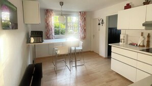 A spacious kitchen with a dining area, wooden flooring, and a view of greenery outside.