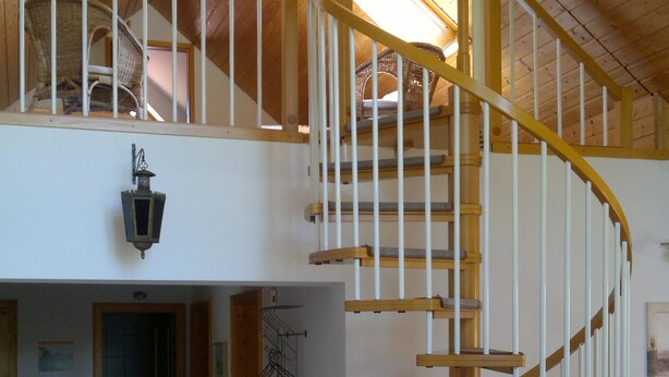 Ein geräumiger Loft mit einer Holztreppe, hohen Decken und Blick auf den oberen Stock.