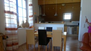 Eine moderne Küche mit Holzausstattung, eine Essecke mit Tisch und Stühlen sowie ein Wohnbereich mit einer Couch.