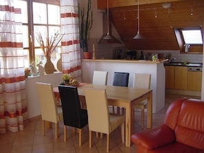 A dining area with a wooden table and chairs, a red sofa, and a kitchen in the background.