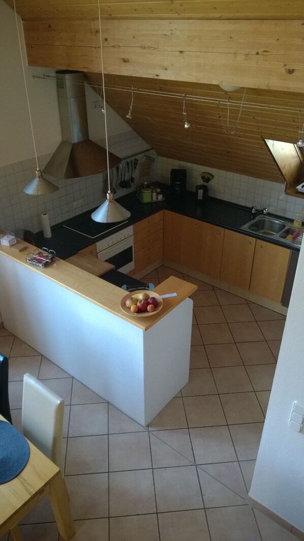 A kitchen with a central island, wooden cabinets, a stove, and hanging pendant lights.