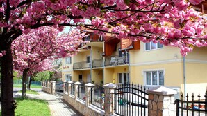 A hotel with a stone wall and black iron fence, surrounded by blooming pink trees. - New, modern apartments, bright, friendly and clean! Many regular guests.  (Hévíz)