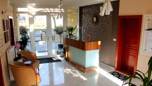 A reception area with a wooden reception desk, two chairs, a clock on the wall, and a red door. - New, modern apartments, bright, friendly and clean! Many regular guests.  (Hévíz)