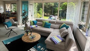 Amplia sala de estar con un sofá modular grande, una mesa de centro y vistas al jardín a través de ventanas grandes.