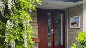 Una entrada residencial con puerta de madera, un banco y plantas en macetas.