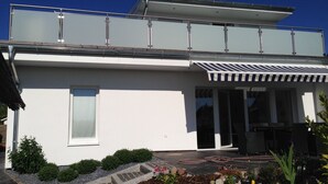 A modern two-story house with a flat roof, large windows, and a covered patio area. - Haus Lena - Holiday near the Baltic Sea including free Wi-Fi (V-DSL) (Pansdorf)